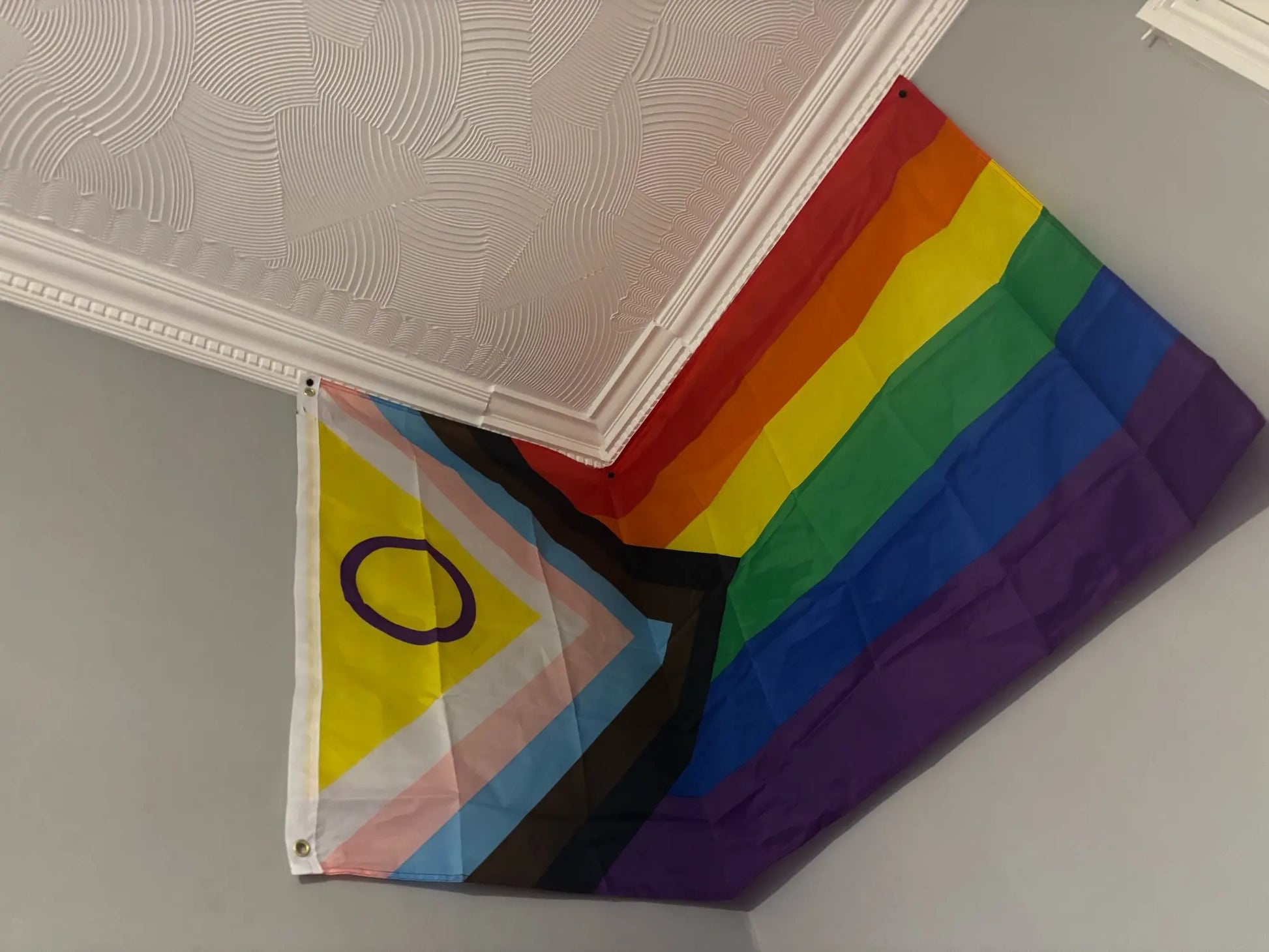 Folded progress pride rainbow flag on a gray surface with a white ceiling.